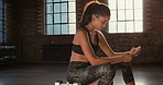 Young hispanic woman thinking and texting on her cellphone at the gym. A fit woman using her cellphone to look for workout routines online. A focused woman cooling down after her exercise routine