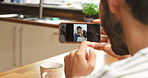 A man looking through photos on his cellphone while sitting in his kitchen in the morning