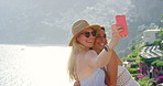 Two happy friends taking selfies on a mobile phone in front of a beautiful view while on holiday in Italy