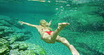 A woman wearing a red bikini on holiday in nature enjoying an underwater swim in a lake. A woman exploring a lake swimming underwater wearing a red bikini