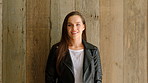 A cheerful young woman standing, posing in front of a wooden wall. A young woman on holiday standing in front of a wooden wall smiling. A happy woman enjoying her holiday standing by a wood wall