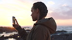 A young woman in pigtails using her smartphone to record videos of the ocean from the promenade at sunset. A young woman on holiday recording the ocean at sunset on her cellphone