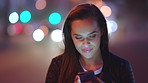 A young woman smiling and reading texts on her cellphone at night out in the city. A woman out at night using her smartphone. A young woman scrolling through apps on her cellphone at night