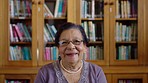 Portrait of a happy senior woman in a library with glasses, knowledge and a positive mindset. Professional, expert and elderly librarian or college professor sitting by bookshelf with education books