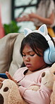 Child, girl and headphones with phone on sofa for games, cartoon streaming or music in living room. Kid, smartphone and confused on couch with elearning, gaming and online education in lounge of home