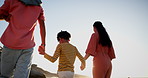 Family, walking and holding hands on beach in sunset for holiday, weekend or outdoor bonding in nature. Mother, father and young child on ocean coast by water in sunshine, travel or stroll by the sea