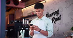 Man, smile and cellphone in coffee shop for communication or online social media, conversation or apron. Male person, smartphone and bakery for customer service or web connection, cafe or internet