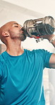 Man, fitness and drinking water at gym for hydration, break or recovery in workout or exercise. Thirsty or tired male person or athlete in rest or breathing with mineral liquid or bottle for health