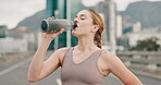 Fitness, running and woman drinking water in city for hydration, rest or recovery from cardio workout. Exercise, street and confident young runner training in urban town with bottle for sports drink