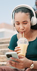 Smoothie, phone and woman with headphones in city networking on social media, mobile app or internet. Happy, technology and young female person drink juice and listening to music on cellphone in town