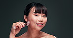 Beauty, massage and jade roller for face with asian woman in studio on dark background for skincare or wellness. Portrait, smile or antiaging and happy young person with product for dermatology