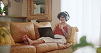 Music, headphones and woman on laptop in living room listening to song, track playlist and radio on sofa. Happy, weekend and person on computer for streaming subscription, podcast and audio in home