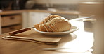 Bread, roll and plate in kitchen for breakfast, meal or morning snack on wooden table. Closeup of interior, wheat or cut slices for cooking, baking or bun for food, nutrition or carbohydrates at home