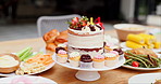 Birthday cake, table and food for event, celebration and party on patio with lunch meal. Dessert, home and outdoor with feast, vegetable and sweet baking with cupcake and sugar snack on a plate