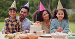 Parents, children and happy with birthday cake in garden with care, love and bonding with food at family home. Father, mother and kids with hat for party, event and embrace at table with celebration