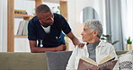 Senior, woman and nurse on sofa with support, conversation and caregiver in living room of retirement home. Elderly, person and black man with kindness, happiness and discussion while reading a book