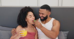 Couple in bed, breakfast together and love, food and happy with man feeding woman strawberry and orange juice. Trust, commitment and nutrition, Valentines day romance and fruit for eating with drink