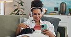 Happy woman, phone and headphones with dog on sofa in relax for listening to music or audio streaming at home. Young female person with smile, animal or pet on mobile smartphone for podcast at house