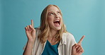 Excited woman, pointing and surprise for advertising, marketing or sale notification on a blue studio background. Portrait of happy female person showing amazing deal, wow or offer on mockup space
