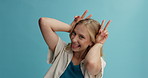 Bunny ears, peace sign and face of woman on blue background for joy, emoji and funny facial expression. Happy, smile and portrait of person with hand gesture for comic, humor and silly in studio