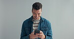 Man, happy or message on cellphone in studio, or notification on mobile app by gray background. Student, positive or typing on cellphone on social media, connection or text for networking in mock up