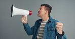 Megaphone, speech and shouting man in studio for broadcast announcement, news or info on grey background. Microphone, noise and frustrated male speaker with message or change, vote or transformation 