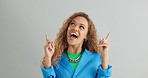 Excited woman, advertising and pointing up with fashion for deal or sale on a gray studio background. Portrait of happy female person or model with smile for notification, alert or offer on mockup