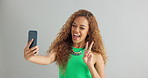 Happy woman, peace sign and selfie with kiss for social media, vlog or memory on a gray studio background. Female person with smile on mobile smartphone for photography or picture on mockup space