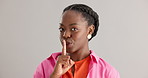 Black woman, secret and smile with finger on lips for whisper or silence on a gray studio background. Portrait of happy African female person, face or looking secretive with gesture on mockup space