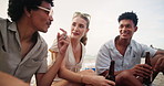 Friends, happiness and talking on beach with beer for bonding, gossip story or relax with picnic in wind. Men, woman and conversation with drinking alcohol, laughing or diversity for social gathering