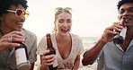 Friends, laughing and talking on beach with beer for bonding, gossip story and relax with picnic in wind. Men, woman or conversation with drinking alcohol, happiness or diversity for social gathering