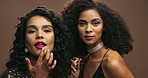 Beauty, makeup and woman friends getting ready for clubbing together in studio on brown background. Portrait, lipstick and happy young people backstage or behind the scenes at nightclub event