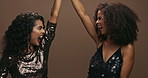 Happy woman, friends and dancing with fashion, makeup or cosmetics for party on a brown studio background. Female person or excited people enjoying fun celebration in stylish clothing for friendship