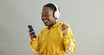Black woman, headphones and smartphone for music with dancing in studio, fun and audio streaming on grey background. Listening to radio playlist, tech and energy with happiness, mobile app and rhythm