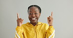 Face, pointing up and black woman with celebration, promotion and excited on grey studio background. Portrait, African person or model with hand gesture, announcement and opportunity with information