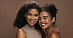 Women, face and happy for beauty in studio for smile, solidarity or care with glow on skin by brown background. Girl friends, people and model for skincare, hug or natural makeup for facial cosmetics
