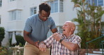 Caregiver, elderly man and outdoor in wheelchair with shoulder pain, helping hand and recovery. Doctor, physiotherapist and senior person with disability, joint or muscle injury in hospital garden