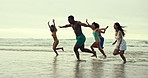 People, diversity and running with water splash on beach for fun holiday, weekend or summer vacation. Group of diverse friends playing and enjoying outdoor nature or freedom on the ocean coast or sea