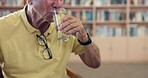 Healthy, hand or old man drinking water for wellness or hydration to relax with arthritis in a library. Parkinson, closeup or thirsty elderly male person with a glass or fresh h2o liquid for vitality