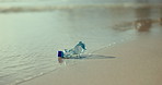Bottle, beach and waste with pollution of recycle plastic, global warming or hazard on ocean coast. Closeup of water or wave with trash, garbage or dirt on sandy shore for recycling on mockup space