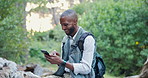 Cellphone, nature and man hiking in forest networking on social media, mobile app or internet. Smile, technology and male person typing on a phone trekking in outdoor woods for exploring or adventure