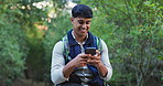 Phone, nature and man hiking in forest networking on social media, mobile app or internet. Smile, technology and male person typing on cellphone trekking in outdoor woods for exploring or adventure.