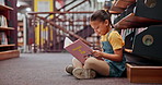 Reading book, kid or girl in a library for a story in school campus for education on bookshelf. Smile, learning or smart child student with scholarship studying knowledge, research or information