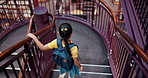 Girl, child and walking in library with bookshelf for research, education and knowledge with school project. Children, student and stairs on campus with books, learning and studying for scholarship