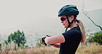 Cyclist, woman and watch in nature for fitness, exercise and outdoor training for marathon by mountain. Healthy athlete, checking and time in helmet for bicycle adventure, cardio and sport to workout