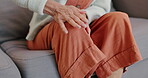 Mature person, knee pain or injury in living room or couch for relaxing, resting and rubbing leg for relief. Hands of woman, health problem and tension on patella or kneecap on a sofa at home