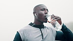 Man, athlete and water for drinking or music in nature, run and training for wellness or fitness for body. Outdoors, podcast and radio with hydrate liquid, African male person in cardio workout