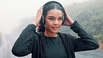 Woman, headphones and running training on mountain road for music playlist, podcast or exercise. Female person, cardio and outdoor endurance in raining weather for commitment, fitness or challenge