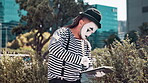 Performance, mime and person in city, creative and outdoor with tablet for acting in circus with costome. Comic, imitator and impressionist with makeup on face for entertainment of art in carnival