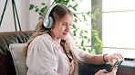 Cellphone, headphones and woman on sofa at house networking on social media, mobile app or internet. Smile, typing and female person listening to music, radio or album on phone in living room at home